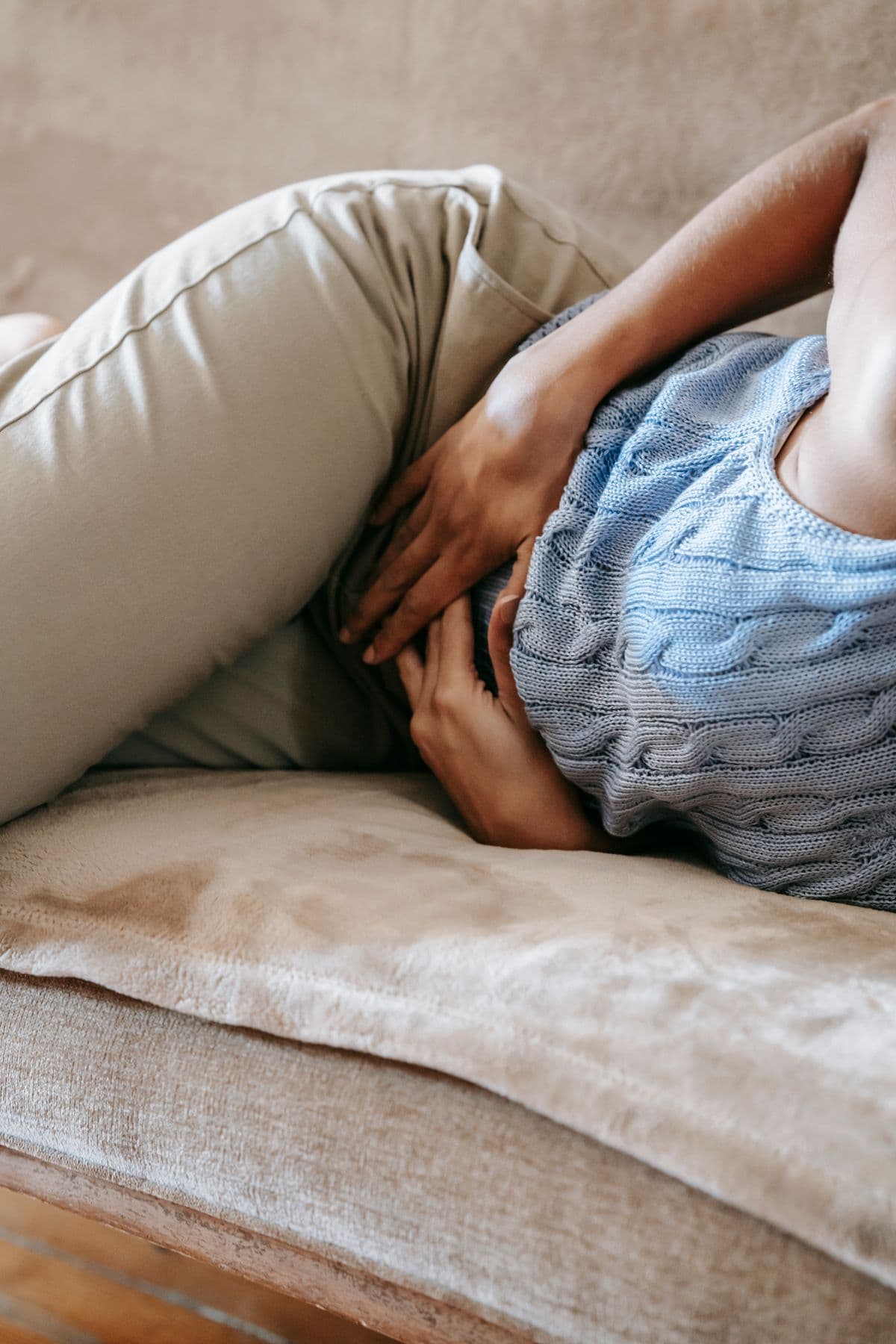 En kvinna i stickad tröja ligger på en soffa och håller händerna mot magen